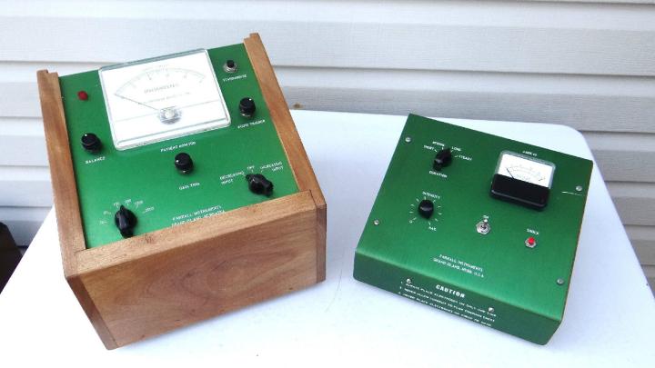 Photo of two visually keyed electric shock devices used in aversion therapy. Both devices have green metallic surfaces. The one on the left has a wooden casing and various switches and buttons that read: "STANDARDIZE," "BALANCE," "AUDIO TRIGGER," PATIENT MONITOR," and a dial from "DECREASING INPUT" to "INCREASING INPUT." There is also a scale measuring direct current in milliamperes. The device on the right has an "ON" switch, a "DURATION" dial, an INTENSITY" dial, and a "SHOCK" button.